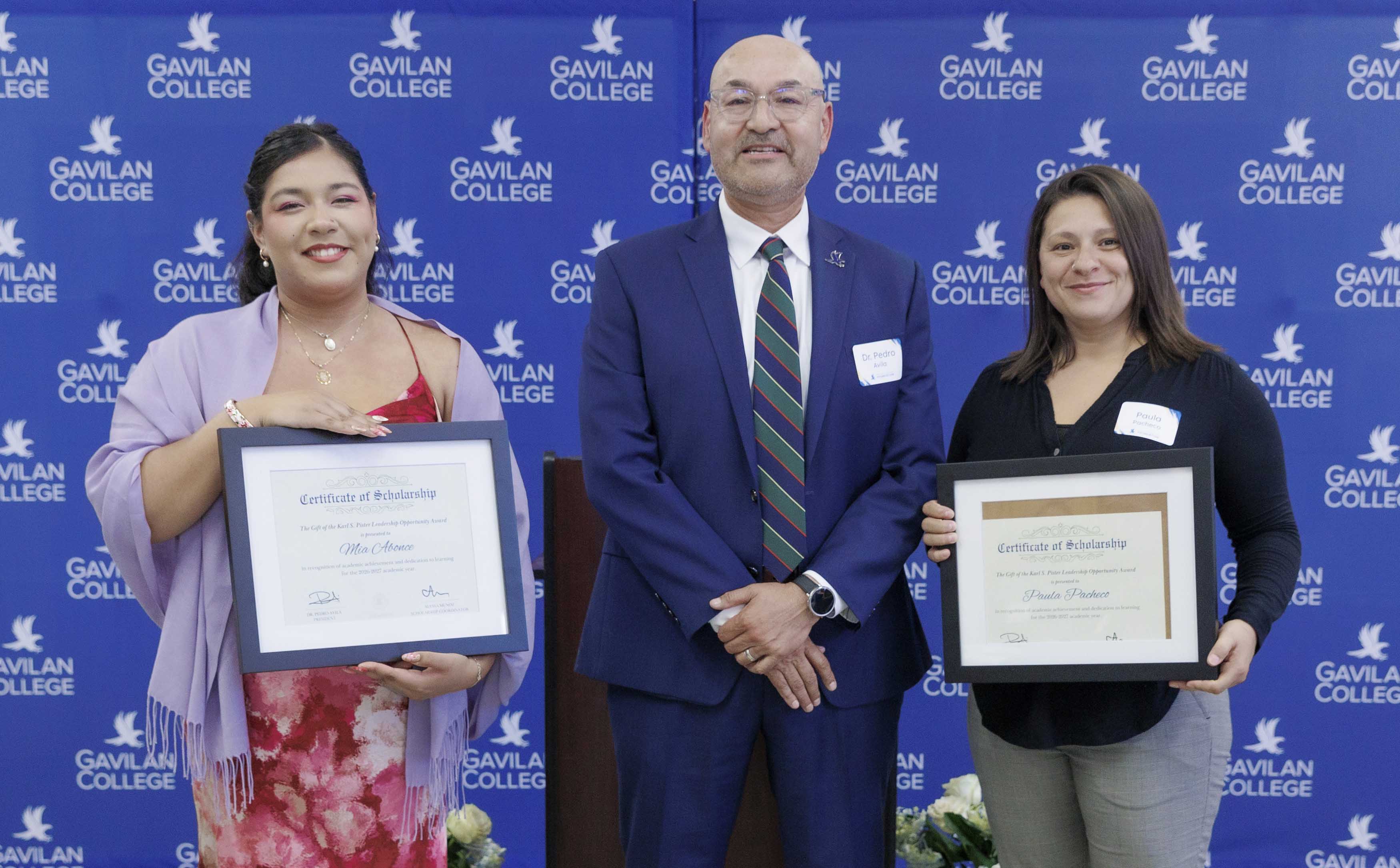 Two students stand on either side of Superintendent President, Dr. Pedro Avila, each holding a framed scholarship certificate, with a blue scholarship event backdrop behind them.