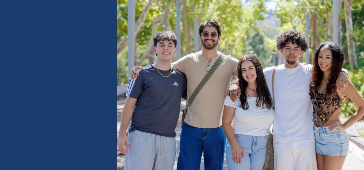 Five people pose together outdoors on a tree-lined campus walkway, smiling at the camera. The group includes three men and two women.