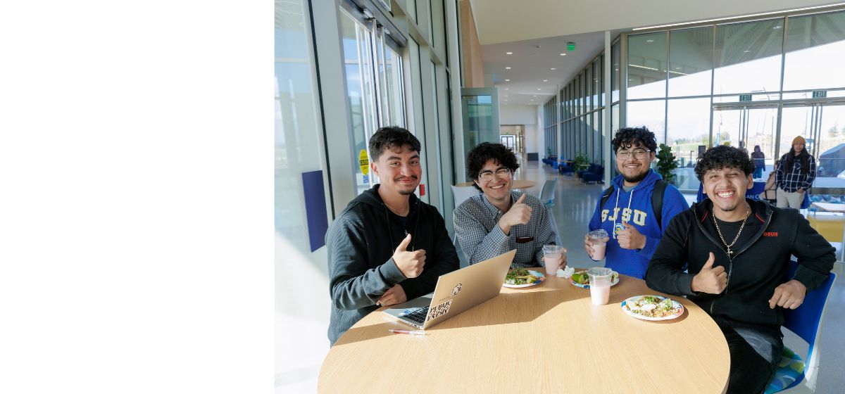 Photo of four male students smiling at a table at the Hollister Campus eating tacos