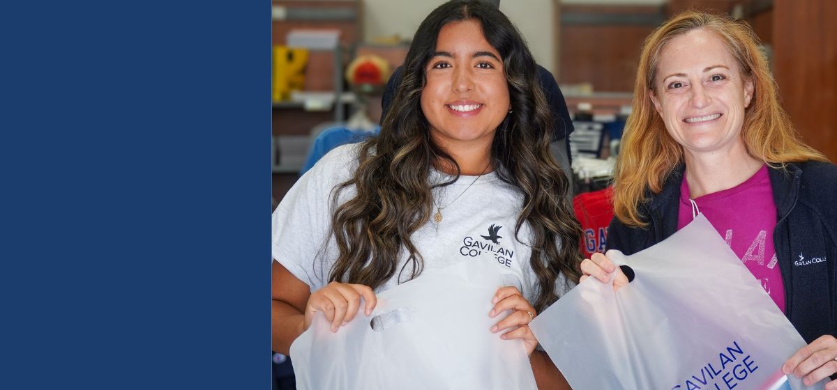 Two females wearing Gavilan College shirts holding plastic Gavilan College bags in front of the bookstore