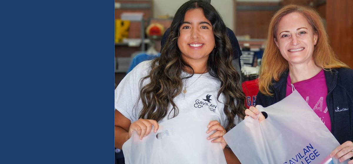 Two females wearing Gavilan College shirts holding plastic Gavilan College bags in front of the bookstore