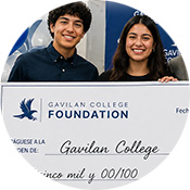Two smiling students stand behind a large ceremonial check featuring the Gavilan College Foundation logo. The image is cropped into a circular design, showing the students from the waist up with part of the oversized check visible in the foreground. The check includes the Gavilan College Foundation branding and is set against an event backdrop.