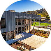 Exterior view of Gavilan College’s Library and Student Resource Center, featuring modern architecture, a blue-gray facade, large windows, and an outdoor plaza with walkways and landscaping.