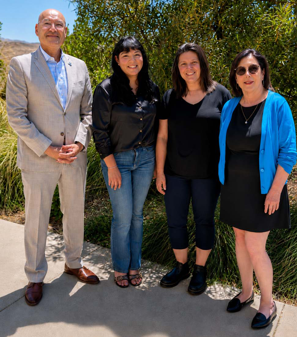 Four people stand outdoors on the Gavilan College campus, smiling at the camera with trees and hills in the background on a sunny day. From left to right are Dr. Pedro Avila, Superintendent/President of Gavilan College; Paula Pacheco; Mia Abonce; and Anna Quinones, Director of the Gavilan College Foundation.